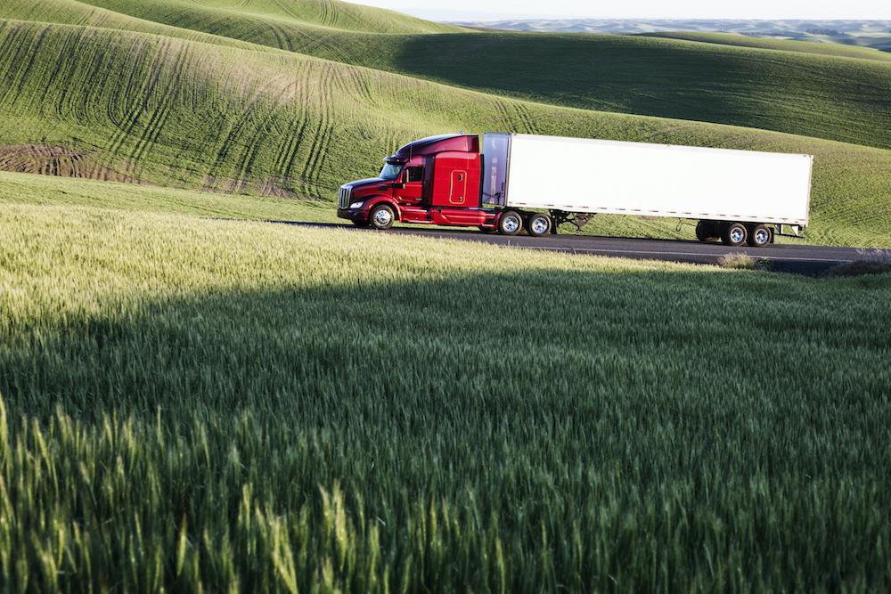 Semi-truck driving on a road through a wheat field